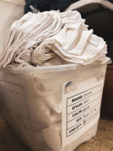 super rush white gildan t shirts folded by size in a plastic bin at a screenprint shop dedicated to fast t-shirt printing